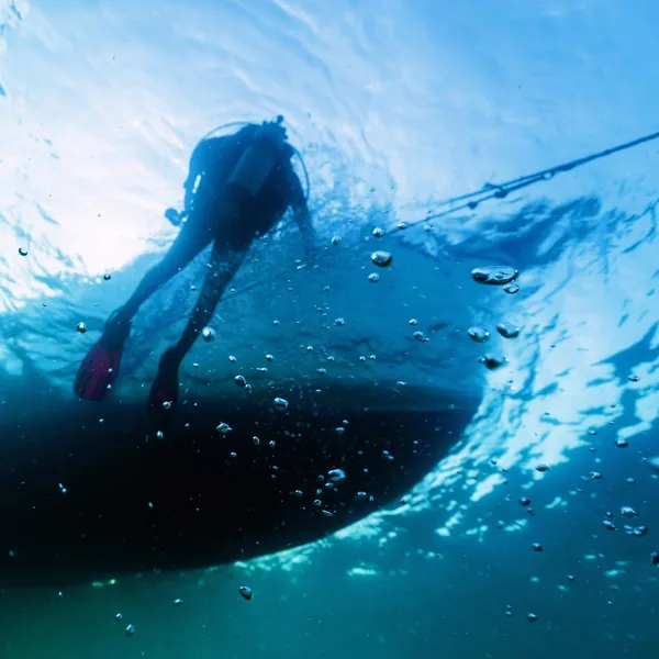 Diver swimming above a boat hull, photographed from underwater